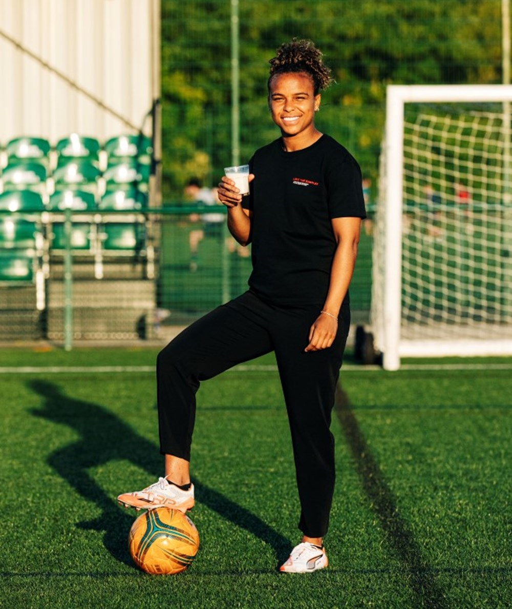 Footballer Nikita Parris holding a glass of milk with her foot on a football